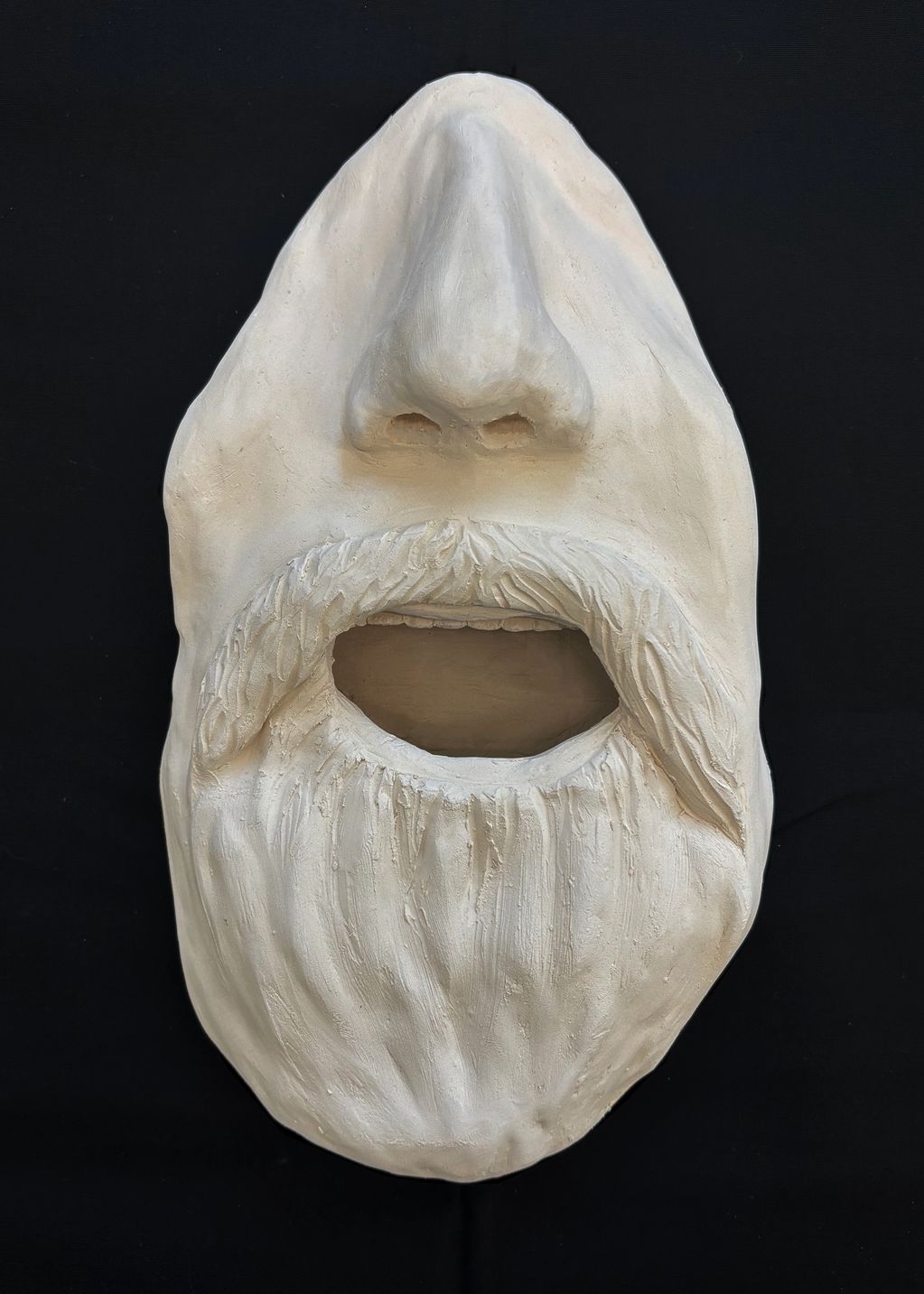 A white sculpture of a bearded face with open mouth on a black background.