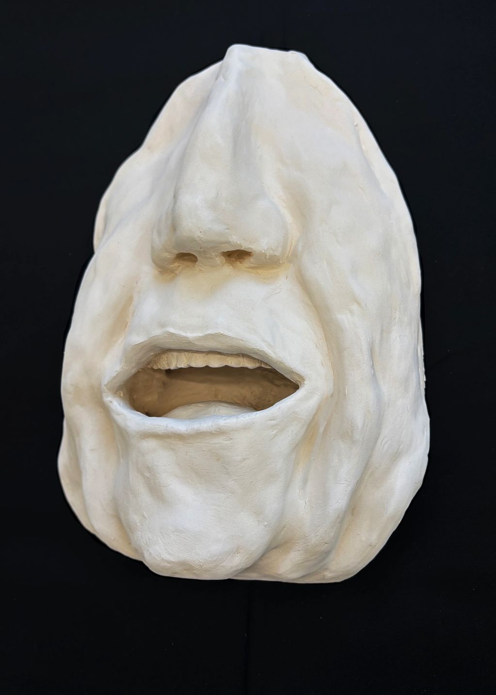 A white sculpture of a human face with an open mouth against a black background.
