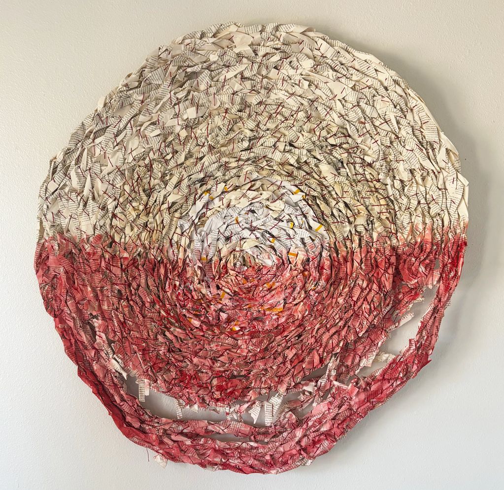 Circular wall art made from layered, crumpled paper with red and white hues.
