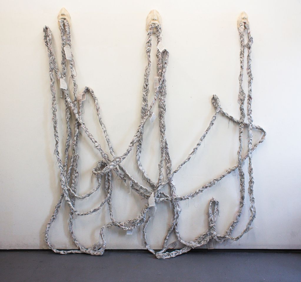 Braided fabric strands hanging from three mask-like hooks on a white wall.
