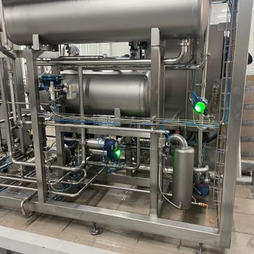 Industrial stainless steel machinery with pipes and gauges in a factory setting.