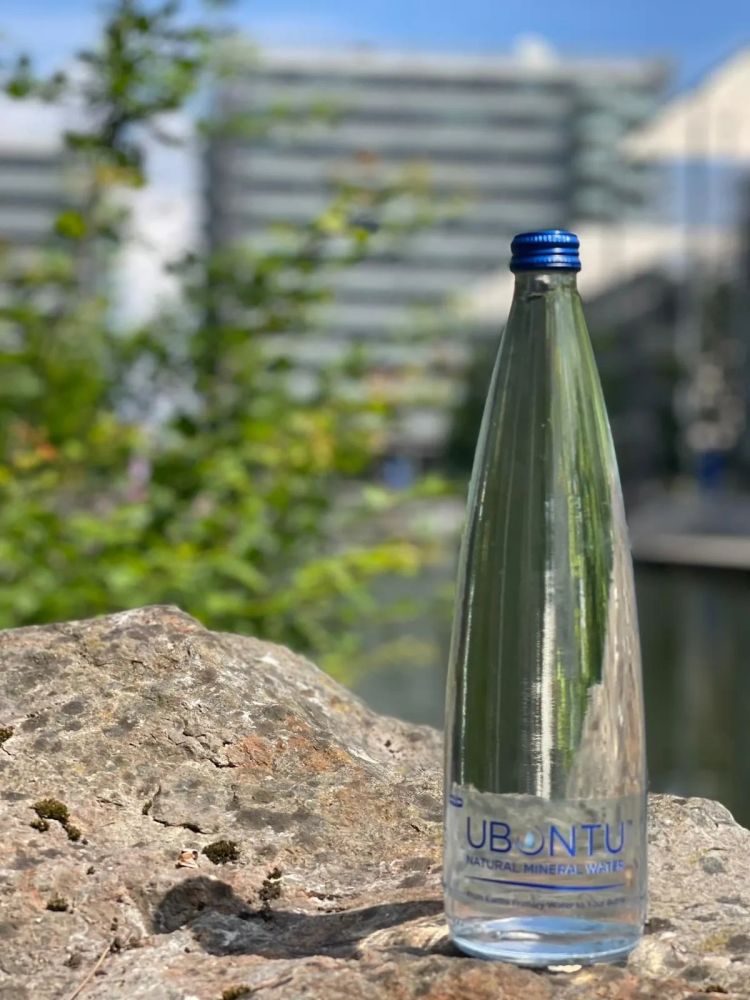 A clear glass bottle of Ubuntu natural mineral water on a rock outdoors.
