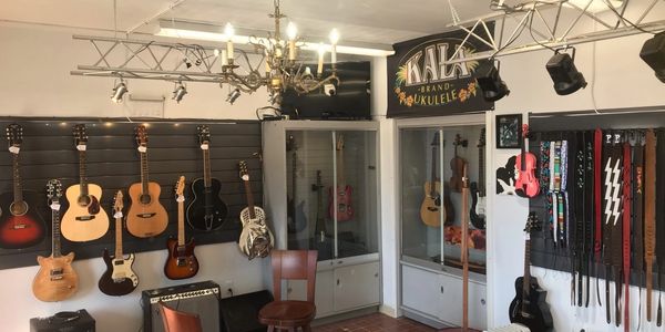 A cozy music store corner with guitars, ukuleles, and straps displayed on walls.
