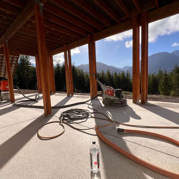 Construction tools on a concrete floor under a wooden structure with mountain views.