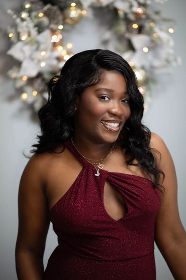 Smiling woman in a sparkling burgundy dress with festive lights in the background.