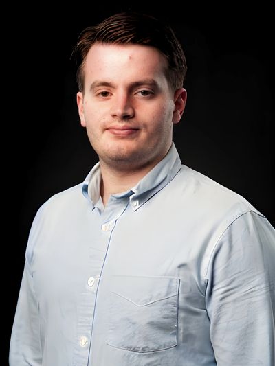 Young man in a light blue button-up shirt against a black background.