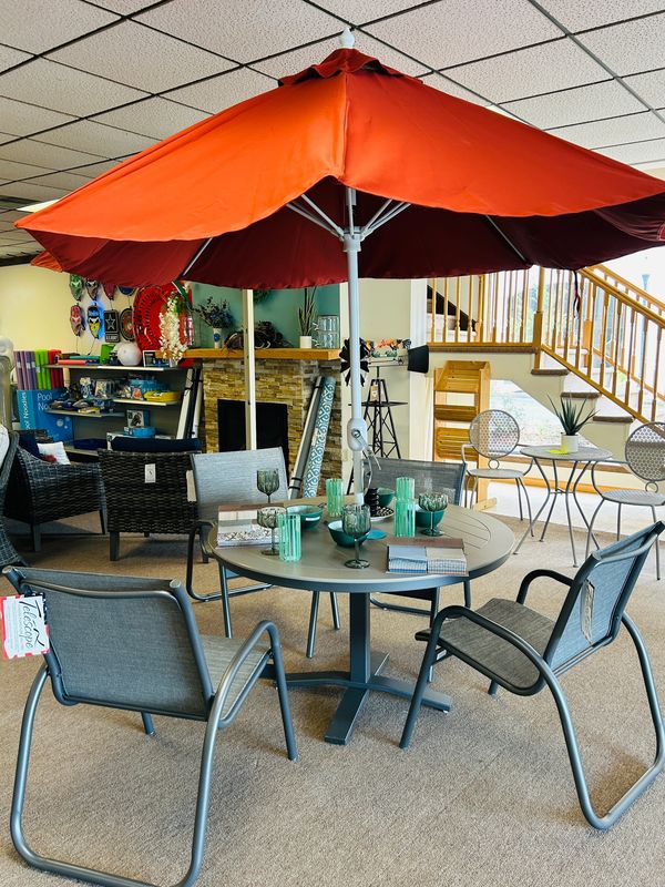 Indoor patio set with orange umbrella and tableware in a showroom.
