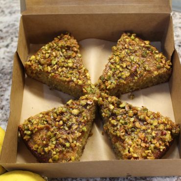 Four nut-covered cake slices in a box with lemons nearby.