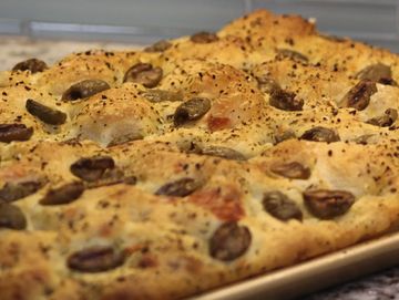Freshly baked focaccia bread topped with olives and herbs on a baking tray.