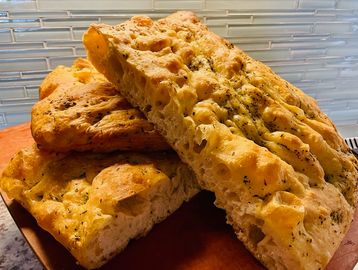 Freshly baked focaccia bread with herbs on a wooden board.