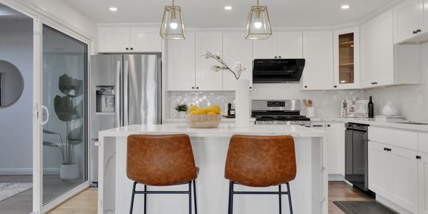 Modern white kitchen with island and brown leather bar stools.