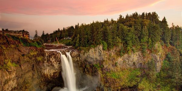 Waterfall cascading down a rocky cliff surrounded by lush greenery at sunset.