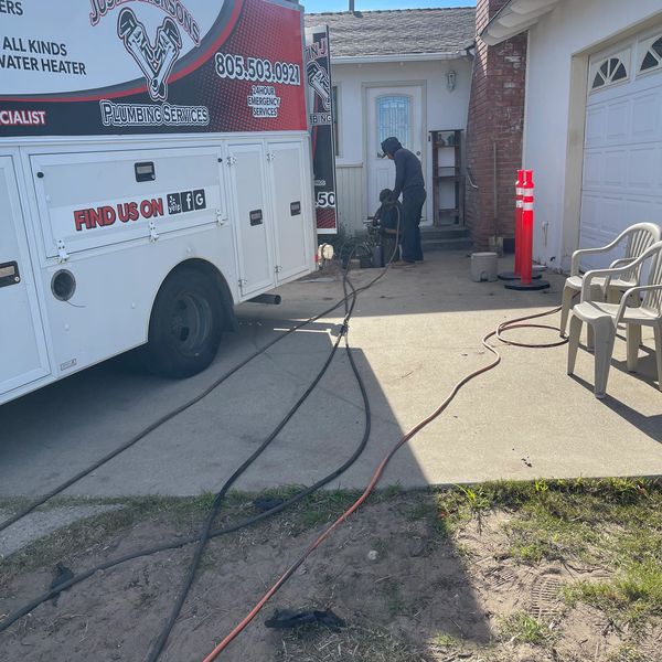Plumber working near a house with hoses and equipment.