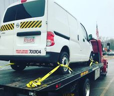 Cargo van and pickup truck being towed down the road in Worcester MA by a flatbed service truck