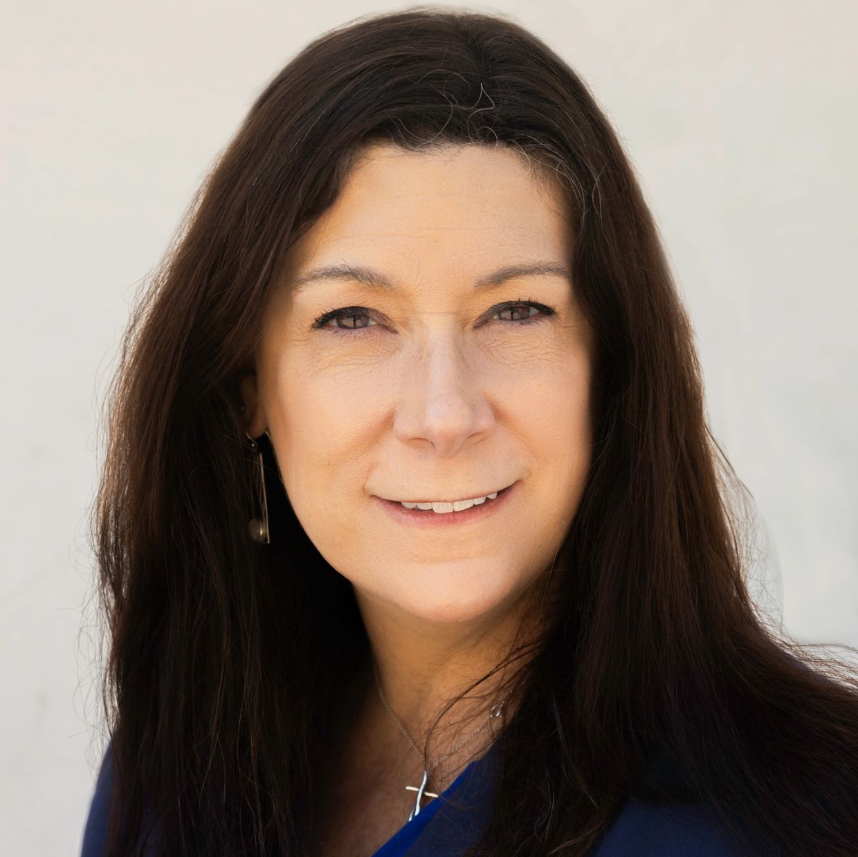 Professional woman with long dark hair wearing a blue blazer and cross necklace.