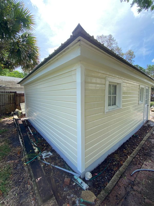 A freshly painted beige and white house corner with a blue foundation and garden hoses around.