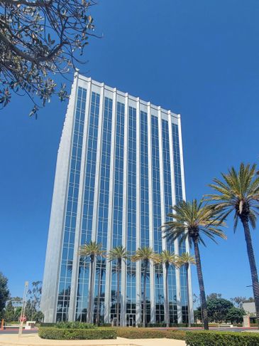Modern glass office building under clear blue sky with palm trees.