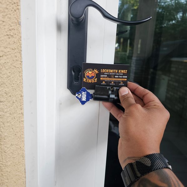 Hand holding a locksmith business card near a door lock cylinder.