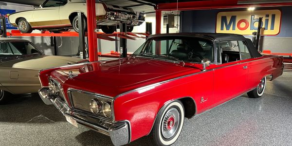 Classic red convertible car displayed indoors with vintage vehicles.