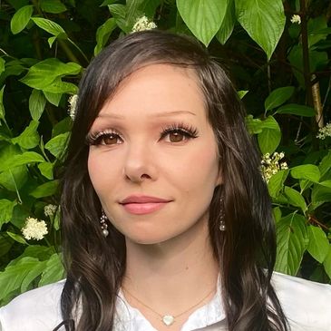 Young woman with long dark hair and makeup standing outdoors.