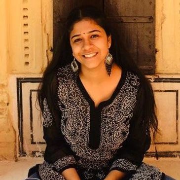 Young woman in black traditional attire smiling warmly.