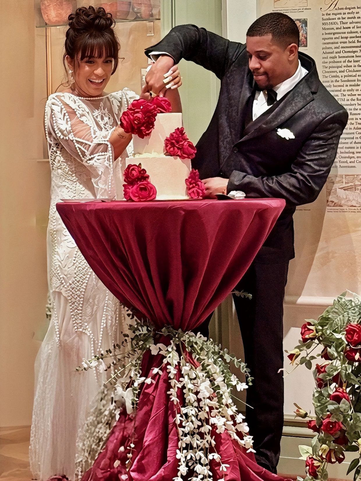 Bride and groom cutting a wedding cake adorned with red roses.