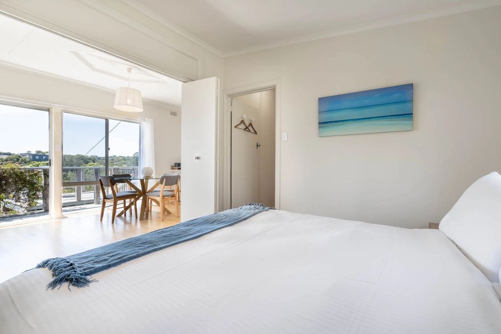 A bedroom featuring a king size bed. The doors are open, leading to a light filled dining room.