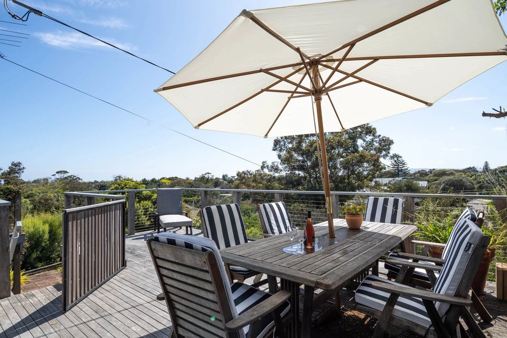 Deck featuring white umbrella, bottle of rosé wine, table and 6 chairs with white and black cushions