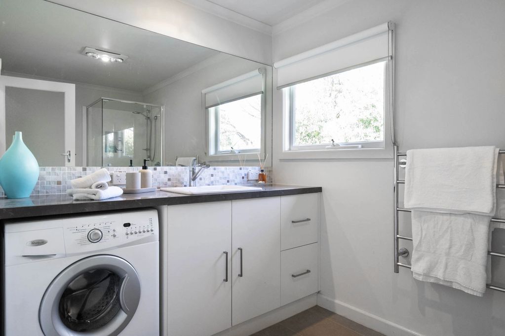 The bathroom sink and cupboards. There is a full width mirror and under counter washing machine.