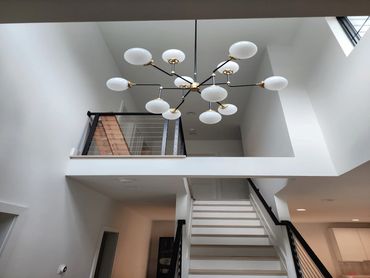Modern chandelier lighting above white staircase.