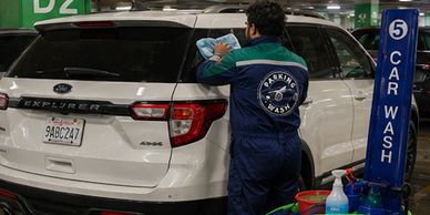 Hombre limpiando la ventana trasera de un SUV blanco en un lavado de autos.