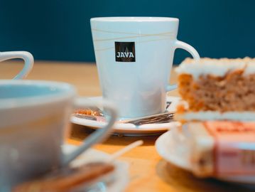 White coffee cups and cake on a wooden table with a blue background.