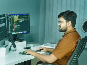Man coding on dual monitors in a modern workspace.