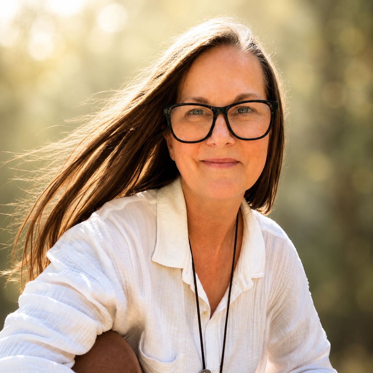 Smiling woman with glasses in a white blouse outdoors.