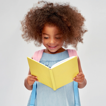 Young girl reading a book while smiling.