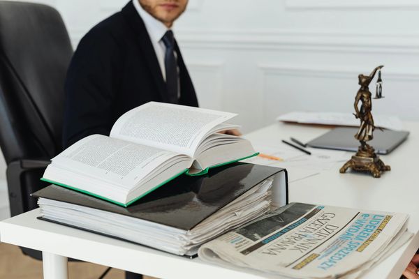 A man in a suit sits behind a desk with law books and a Lady Justice statue.