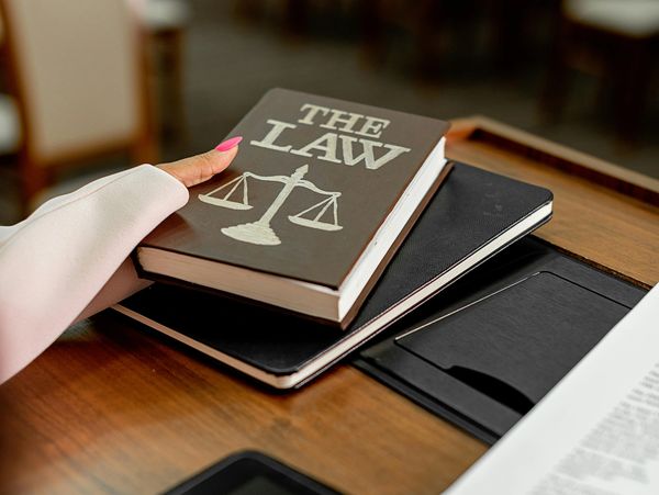 Person holding a law book with scales of justice symbol on a desk.