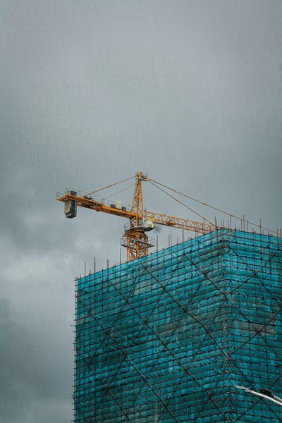 Construction crane atop a building covered in blue scaffolding under a cloudy sky.