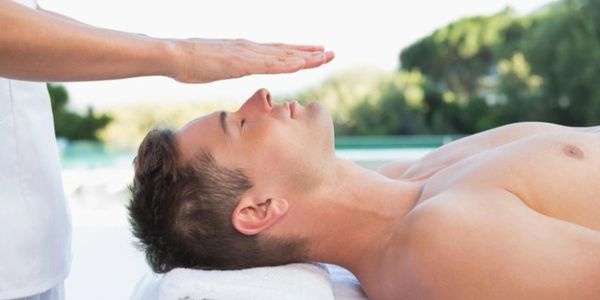 A man receiving energy healing with a hand hovering above his head.