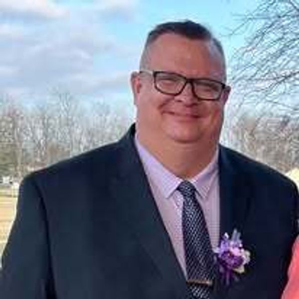 Man in suit with glasses smiling outdoors.