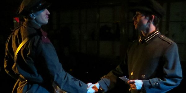 Two men in military uniforms shaking hands in a dimly lit setting.
