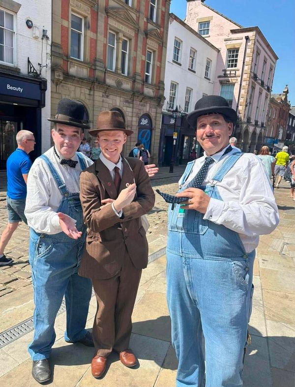 Three men in vintage outfits and bowler hats posing on a sunny street.