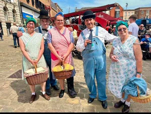 Group of people in vintage clothing holding baskets at an outdoor market event.