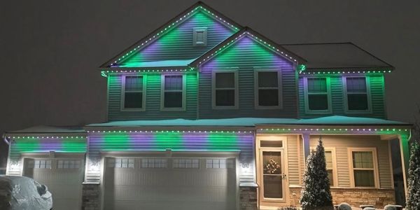 Two-story house decorated with green and purple lights on a snowy night.