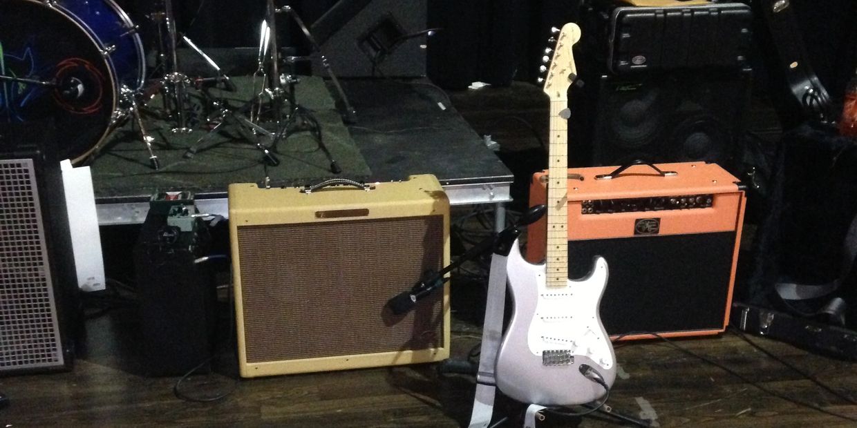 Electric guitar with two amplifiers on a stage floor.