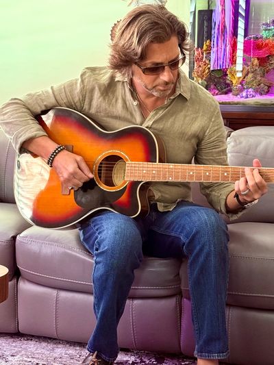 Man playing an acoustic guitar while seated on a couch.