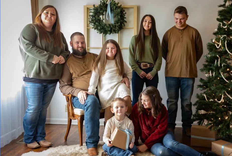 A family gathers for a cozy Christmas photo with a decorated tree and gifts.