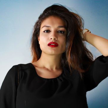 Confident woman with red lipstick and black dress against a light blue background.