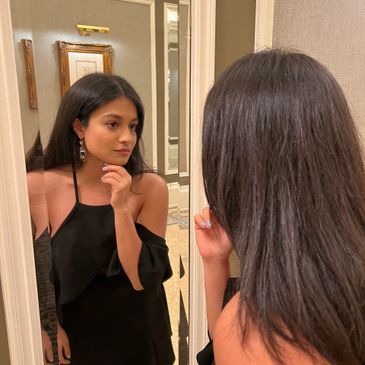 Young woman in a black dress looking thoughtfully into a mirror.
