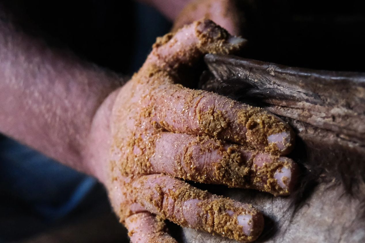 Hand covered in clay or soil working on pottery.